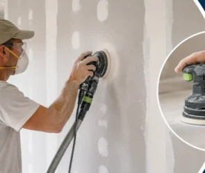 Blog featured image guide on sanding drywall with an orbital sander, showing a worker wearing safety glasses and a respirator mask using a handheld random orbital sander with a vacuum hose attachment on a mudded wall seam, with a close-up inset of the sanding pad.