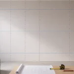 Blog featured image for a drywall layout guide, showing a gridded schematic blue chalk line grid over a large hung drywall room wall, with a blueprint scroll, tape measure, pencil, and stacks of plasterboard panels positioned in the foreground foreground.