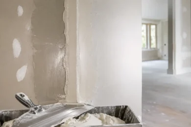 Blog featured image guide on how long does drywall mud take to dry, showcasing a freshly mudded corner wall seam with a clear contrast between wet dark grey joint compound and dry lighter patches, alongside a mud pan and taping knife in the foreground.